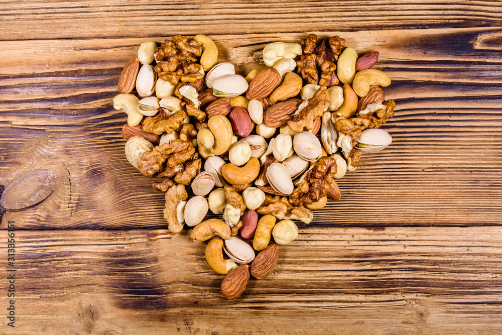 Various nuts (almond, cashew, hazelnut, pistachio, walnut) in shape of heart on a wooden table. Vegetarian meal. Healthy eating concept