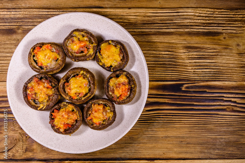 Baked champignons stuffed with minced meat and cheese in plate on a wooden table. Top view