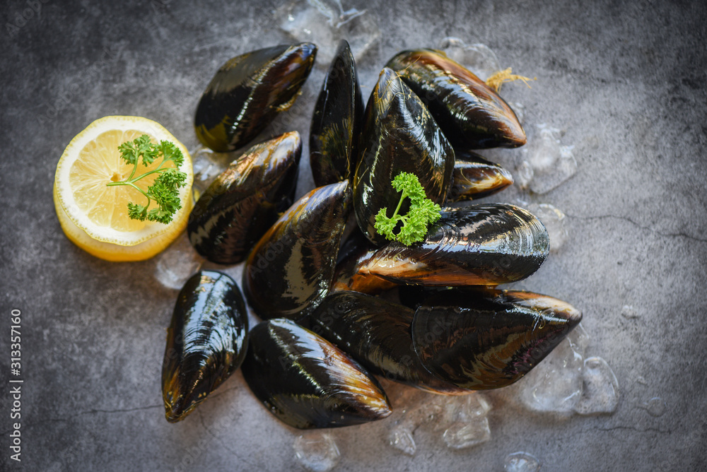 Raw Mussels with herbs lemon and dark plate background - Fresh seafood shellfish on ice in the restaurant or for sale in the market mussel shell food Raw Mussels with herbs lemon and dark plate background - Fresh seafood shellfish on ice in the restaurant or for sale in the market mussel shell food