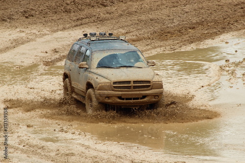 Big power American 4WD car in muddy puddle on dirt off road track, front view