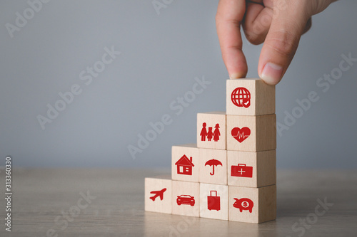 Hand arranging wood block stacking with icon insurance: car, real estate and property, travel, finances, health, family and life, insurance concept.