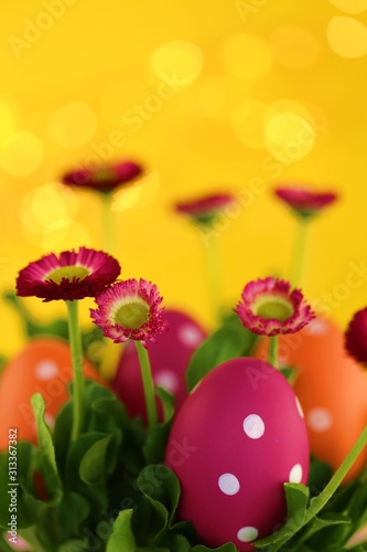 Easter holiday. Pink and orange  eggs in pink daisies colors on a bright yellow background with golden bokeh.Easter religious festive spring background.