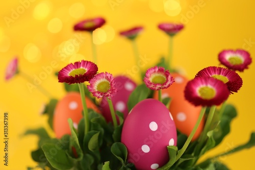 Easter holiday. Pink and orange easter eggs in pink daisies colors on a bright yellow background with golden bokeh.Easter religious festive spring background.