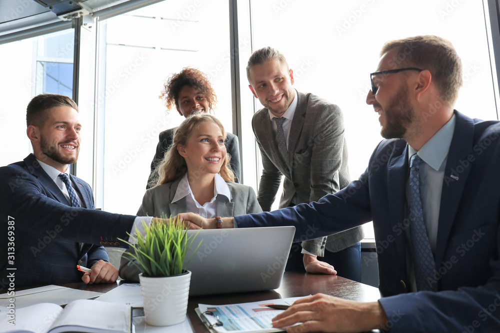 Young modern businessmen in formalwear shaking hands and smiling while working in the office Young modern businessmen in formalwear shaking hands and smiling while working in the office