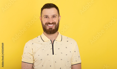 Smiling bearded young male model dressed casually, isolated over yellow background.