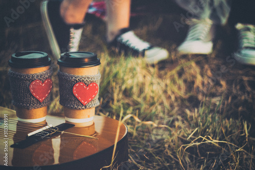 Romantic couple hugging while having picnic in sunset light. Coffee cup cozy knitted sleeve with felt red heart.