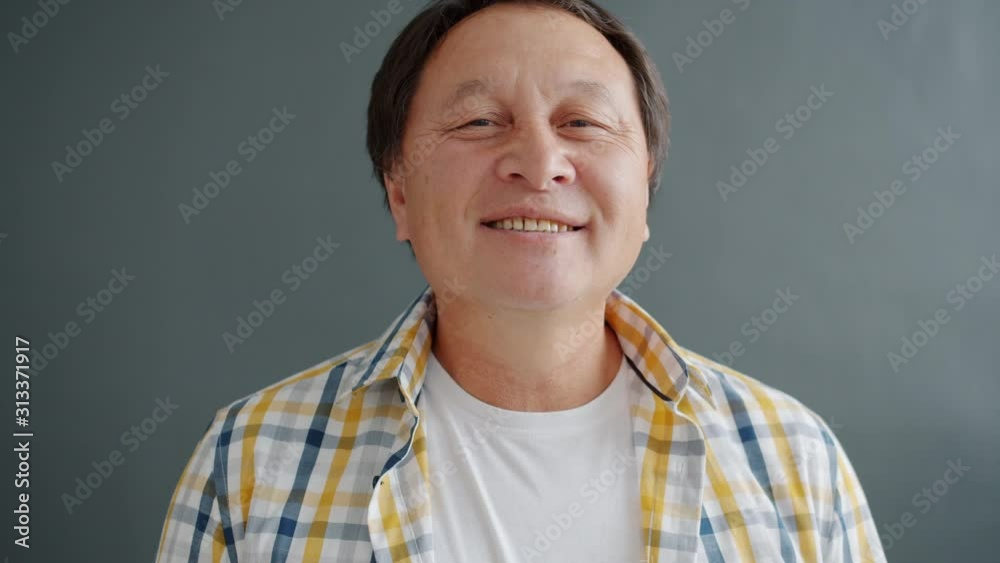 Happy Asian man smiling with toothy smile feeling cheerful and carefree standing alone on gray background. Joyful people and positive emotions concept. Happy Asian man smiling with toothy smile feeling cheerful and carefree standing alone on gray background. Joyful people and positive emotions concept.