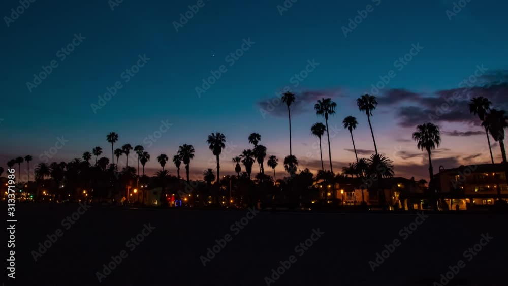 Time lapse in motion or hyper-lapse of sun setting over Santa Barbara beach in California with coastline and palm trees.