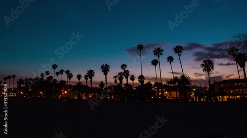 Time lapse in motion or hyper-lapse of sun setting over Santa Barbara beach in California with coastline and palm trees.