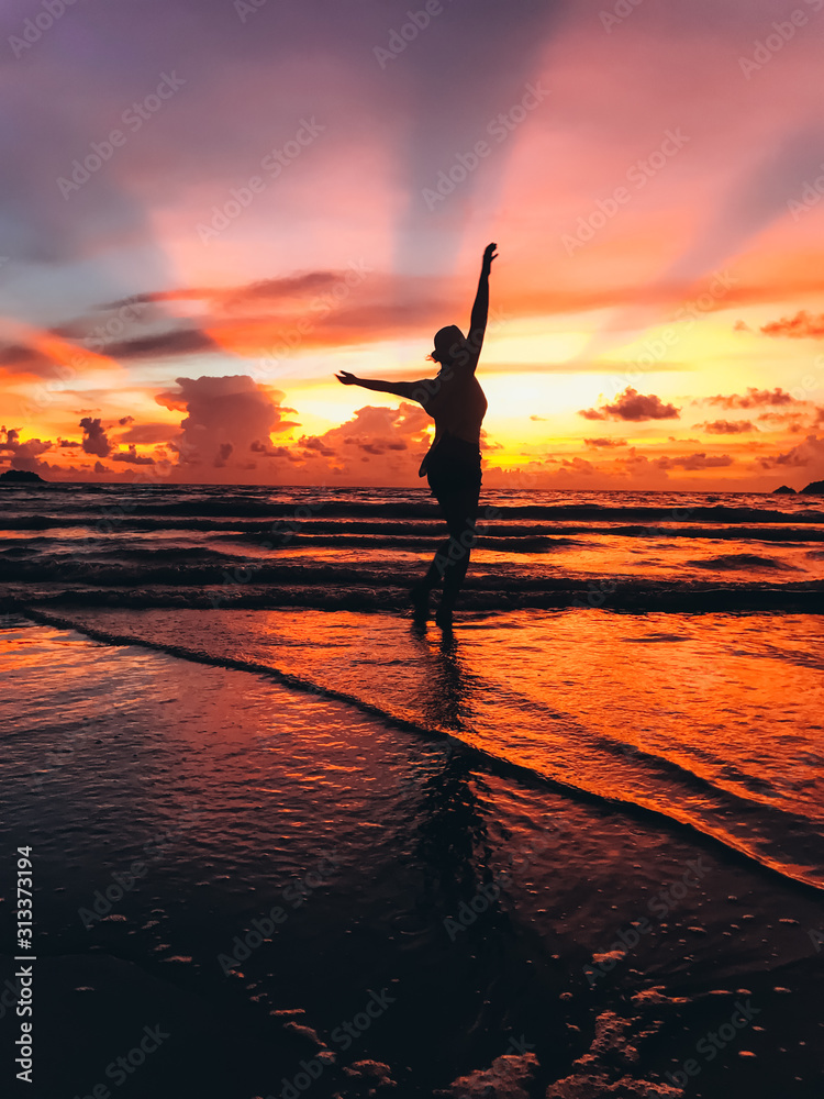 A beautiful young woman is dancing on the seacoast on the background of sunset. Sense of freedom. Amazing mesmerizing landscape