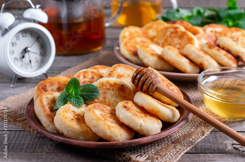 Cottage cheese pancakes, syrniki with honey on a plate on wooden background