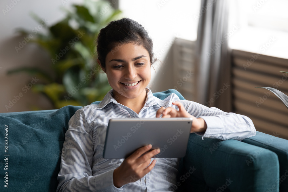 Happy indian woman using tablet sit on sofa at home - obrazy, fototapety, plakaty 