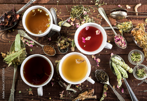 Assortment of cups of tea and dry tea in spoons on a wooden background. Top view.