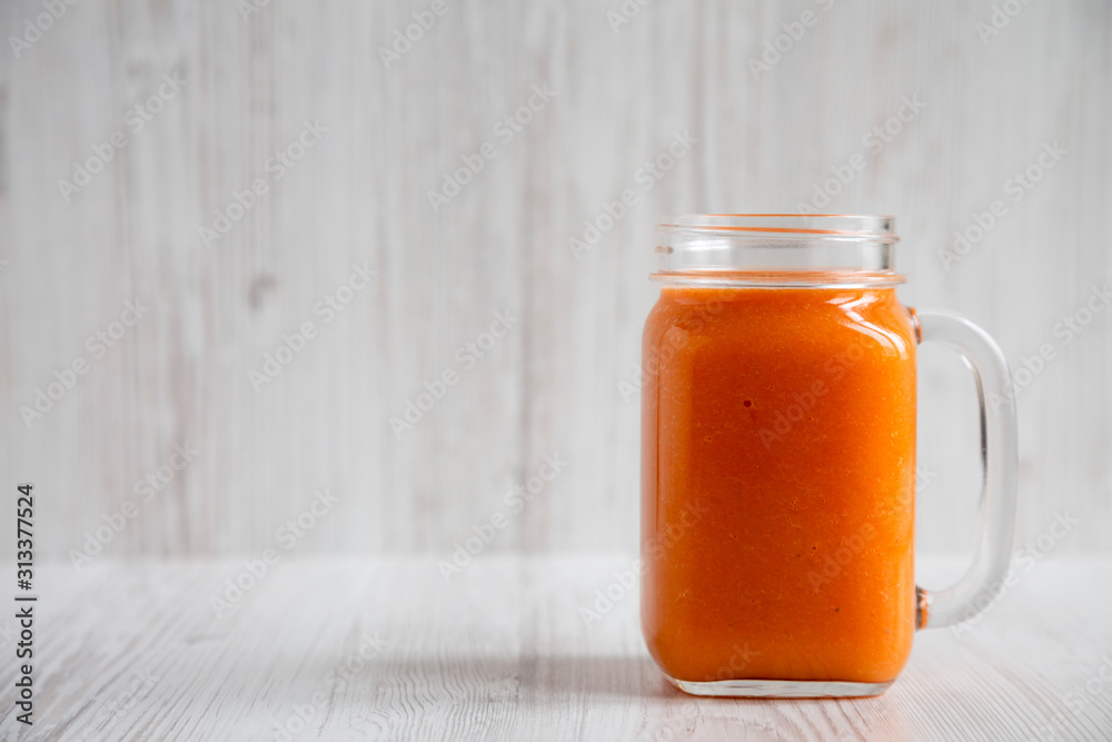 Homemade Mango Carrot Smoothie in a glass jar mug over white wooden background, side view. Copy space. Homemade Mango Carrot Smoothie in a glass jar mug over white wooden background, side view. Copy space.