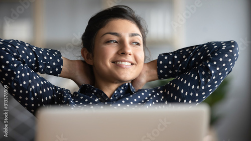 Happy satisfied indian woman relax with laptop looking away dreaming