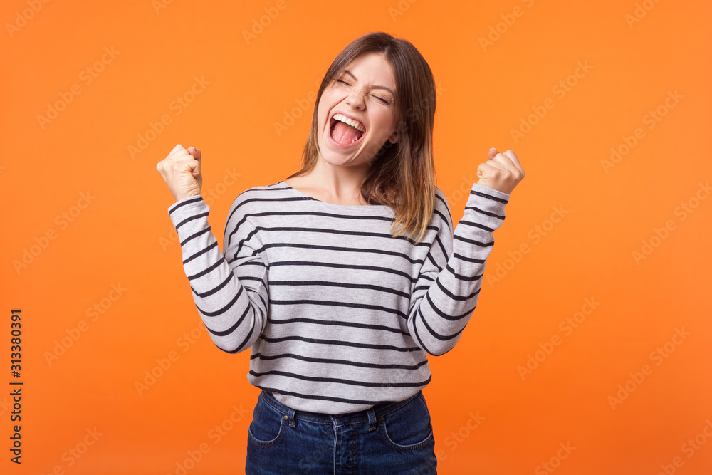 Φωτογραφία Yes I did it! Portrait of joyous winner, young woman with brown hair in casual shirt standing with clenched fists and closed eyes, celebrating victory