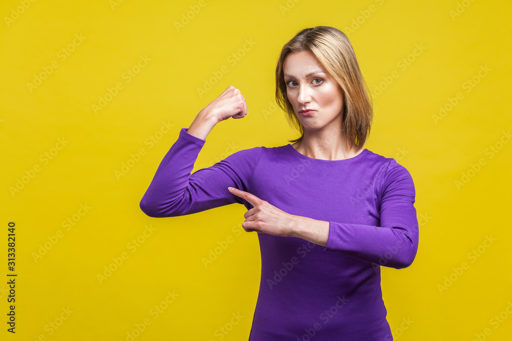 I'm strong. Portrait of proud successful businesswoman in elegant purple dress pointing at biceps proud of herself, being independent and confident, feminism. studio shot isolated on yellow background I'm strong. Portrait of proud successful businesswoman in elegant purple dress pointing at biceps proud of herself, being independent and confident, feminism. studio shot isolated on yellow background