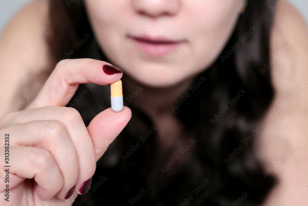 Obraz premium Girl taking pill, woman with capsule in hand close up. Concept of illness and health care, taking medication, vitamins for beauty, slimming