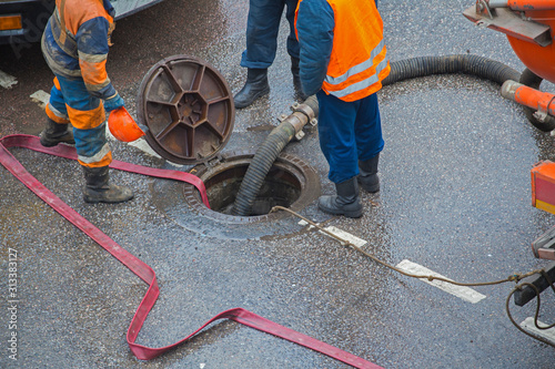 Repair work on troubleshooting or communal service work. Open iron hatch with cable going inside.  Repair on networks of water supply, heating. The hatch is open. The pipe repair. Special machinery.