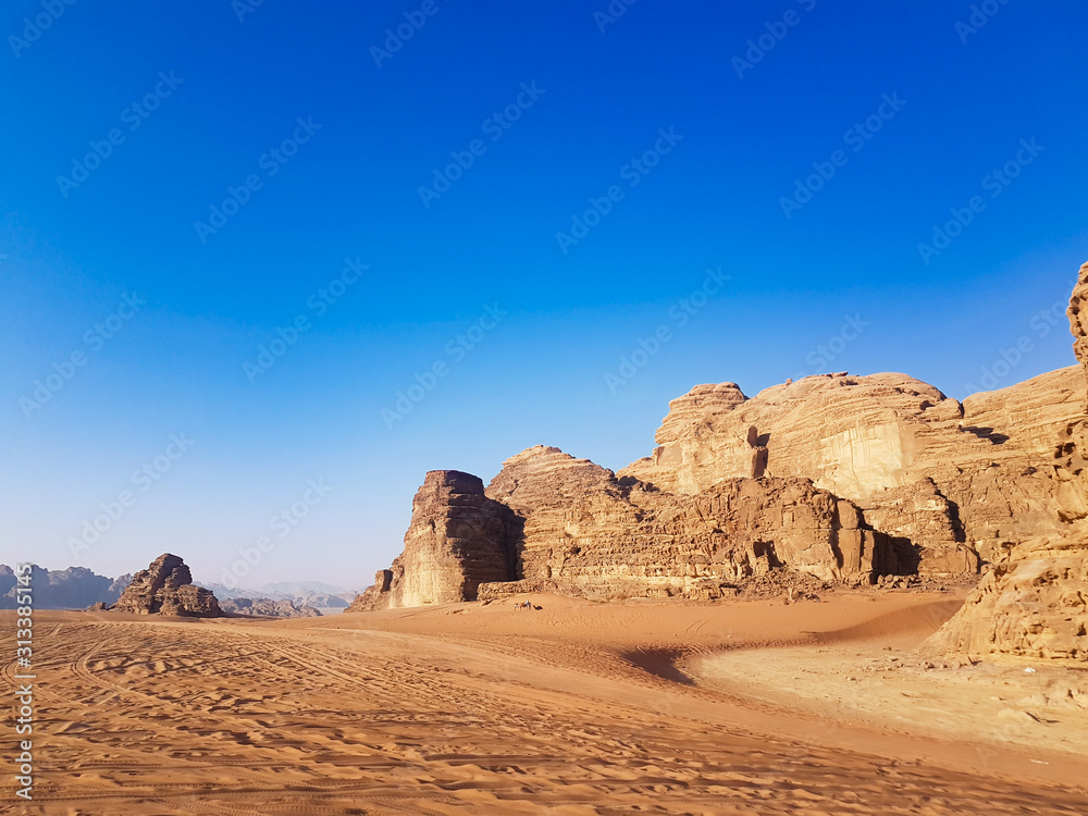 Safari trip on a pick-up truck around the Wadi Rum desert on a sunny day with a blue sky. Off-road cars that left their tire tracks on the sand among rocky mountains in the Arabian desert. Safari trip on a pick-up truck around the Wadi Rum desert on a sunny day with a blue sky. Off-road cars that left their tire tracks on the sand among rocky mountains in the Arabian desert.