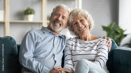 60s loving couple sitting in living room posing looking at camera