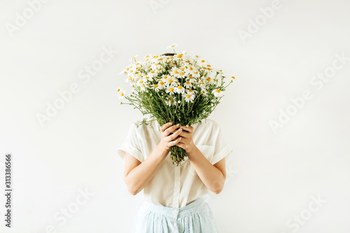 Young pretty woman with bouquet of white chamomile daisy flowers on white background.