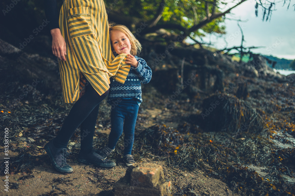 Naklejka premium Toddler grabbing his mother's dress by the river in autumn