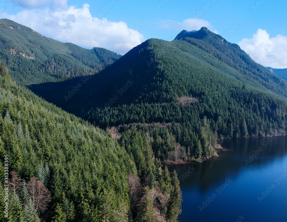 Rarely seen beautiful aerial photographs of Calligan Lake in Washington State with green mountainside open vistas clouds blue sky and shoreline on a warm autumn day.