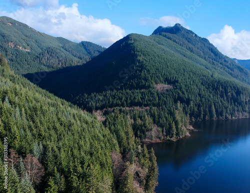 Rarely seen beautiful aerial photographs of Calligan Lake in Washington State with green mountainside open vistas clouds blue sky and shoreline on a warm autumn day.