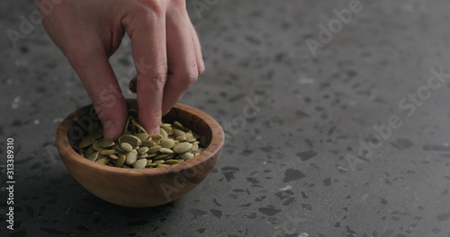 man hand takes pumpkin seeds from olive bowl with copy space photo