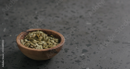 pumpkin seeds in olive bowl on terrazzo countertop with copy space