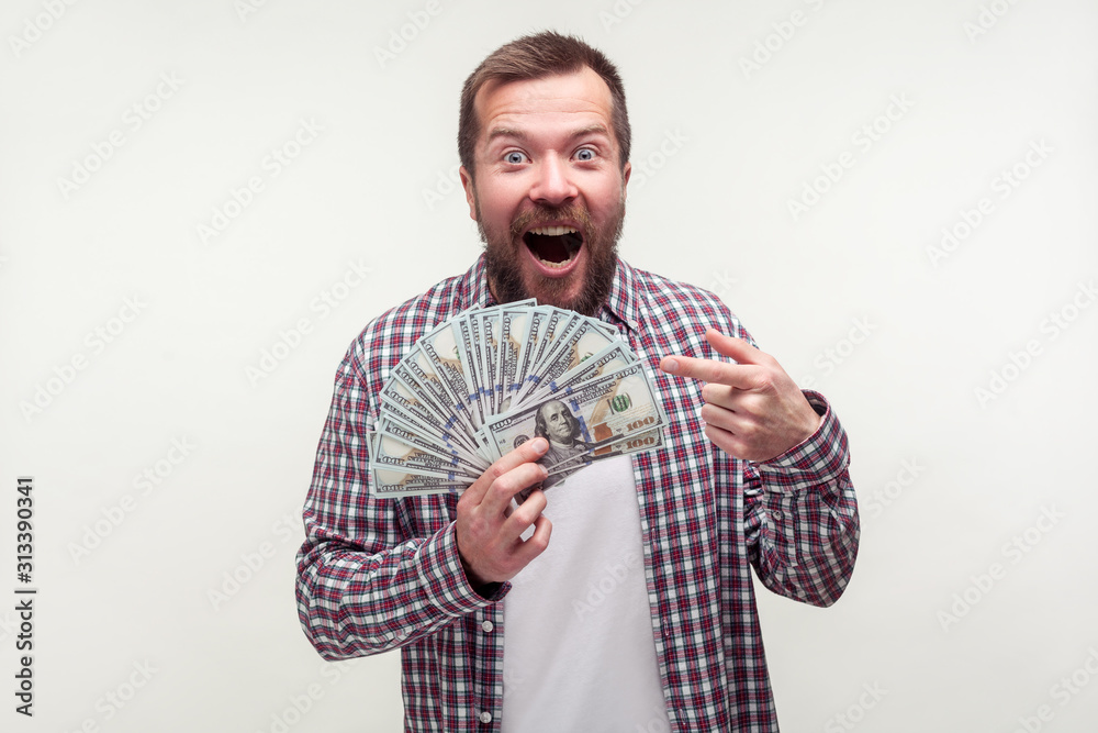 Portrait of amazed satisfied bearded man in casual plaid shirt pointing at dollar banknotes, pleasantly surprised with lottery win, bonus to salary. indoor studio shot isolated on white background Portrait of amazed satisfied bearded man in casual plaid shirt pointing at dollar banknotes, pleasantly surprised with lottery win, bonus to salary. indoor studio shot isolated on white background