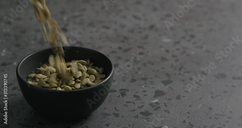 dried pumpkin seeds falling into black bowl on terrazzo countertop
