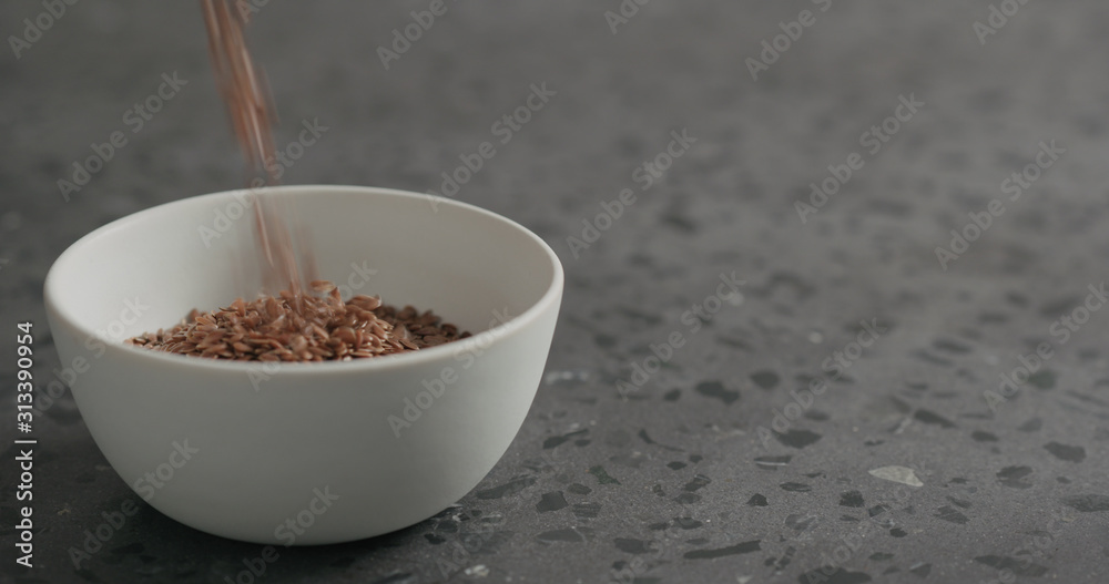 flaxseed falling into white bowl on terrazzo countertop flaxseed falling into white bowl on terrazzo countertop