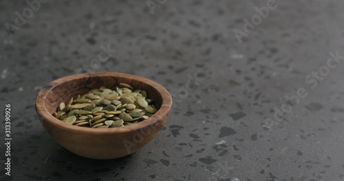 pumpkin seeds in olive bowl on terrazzo countertop with copy space