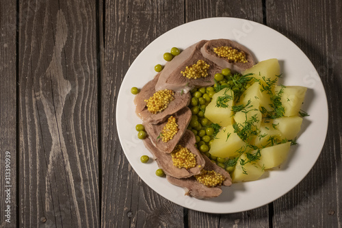 boiled beef tongue with potatoes, green peas, herbs and mustard on dark wooden background 