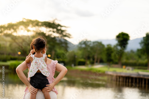 Mother and daughter sitting during sunset hour looking at beautiful landscape. © tienuskin