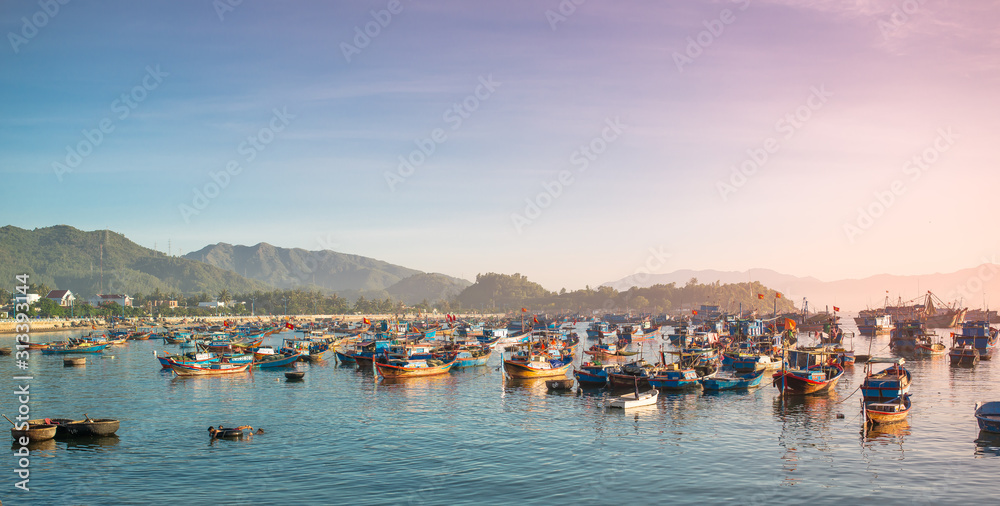 Early morning. The sun only rises above the horizon. In the sea bay, near the coastline, many fishing boats float. All of these boats have recently returned from the sea from nightly fishing. Vietnam.