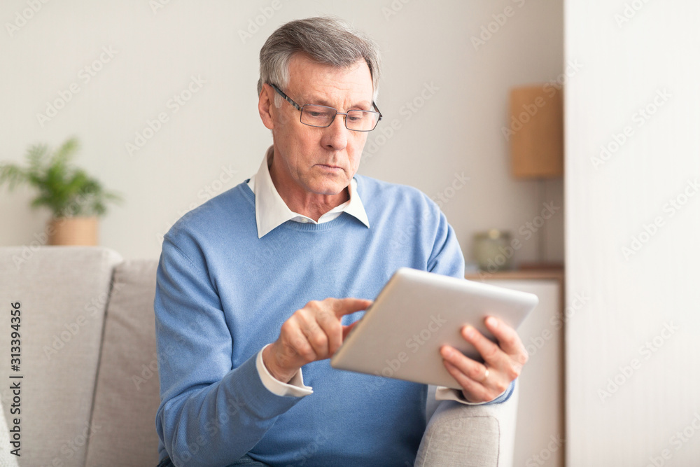 Elderly Man Using Tablet Browsing Internet Sitting On Couch Indoor Elderly Man Using Tablet Browsing Internet Sitting On Couch Indoor