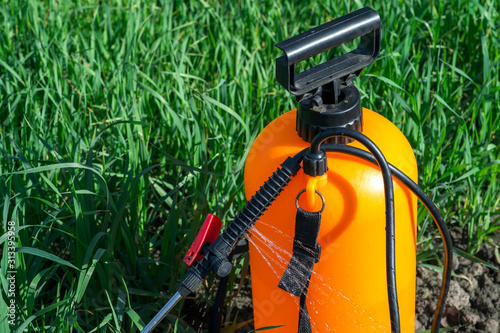 Jets of aqueous chemical solution gush from the black plastic handle of the orange sprayer. Background. photo