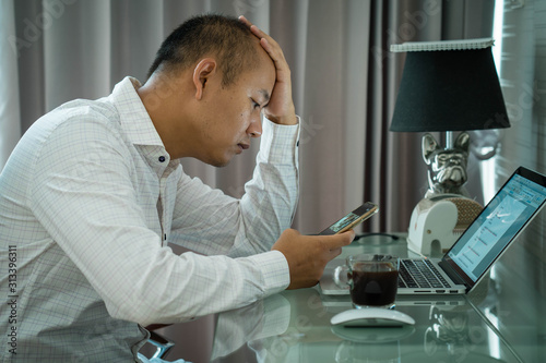 Strain expression face Asian man working at home using laptop and smartphone during lockdown.