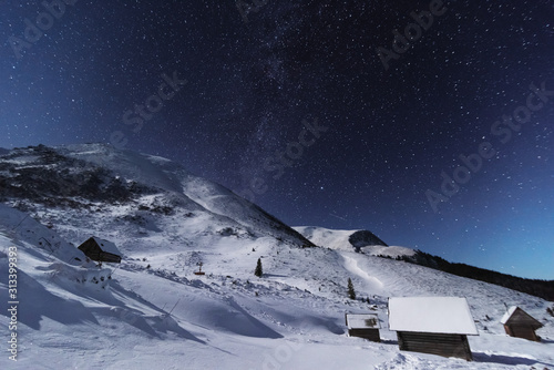 Fairytale landscapes of the winter Carpathian Mountains with a charming milky way in the sky tourist tents and snowy houses in the valleys	