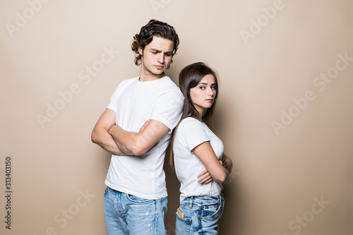 Offended guy and girl wearing beige t-shirts resenting and acting like arguing couple standing back to back with arms crossed isolated over beige background