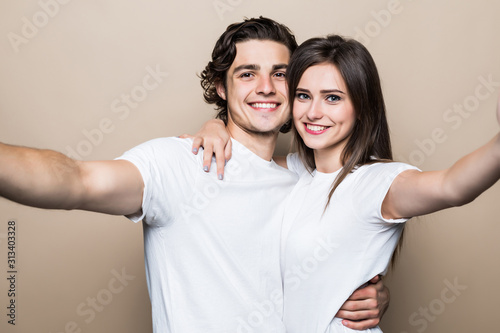 Joyful young loving couple taking selfie on camera, kissing lover isolated on beige background