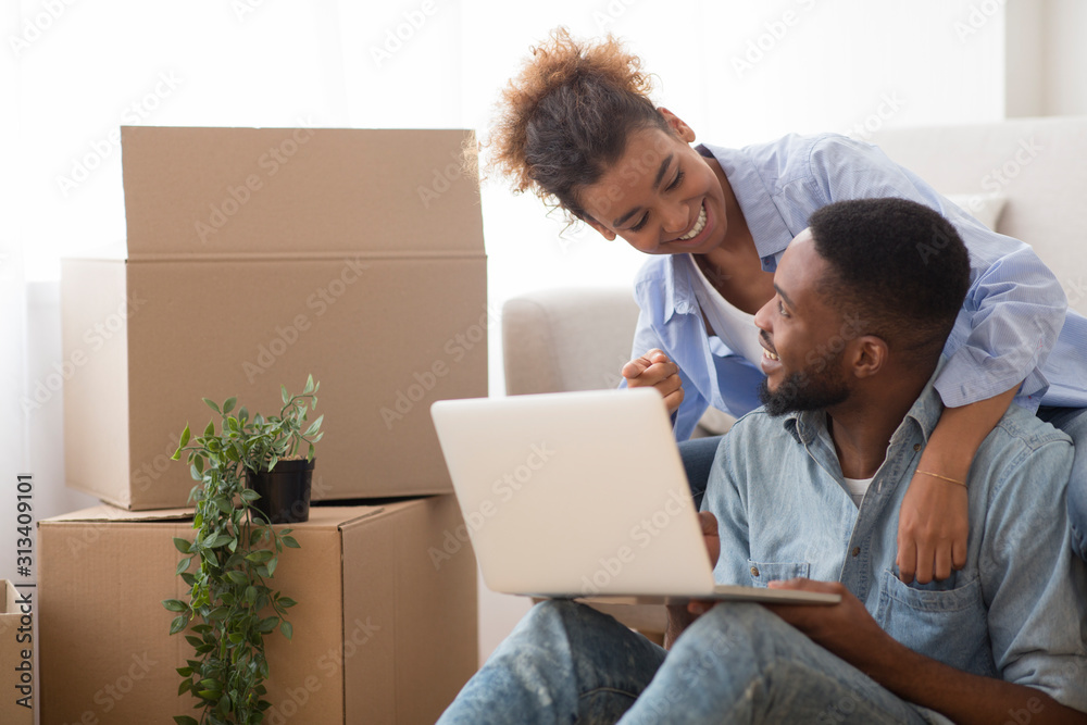 Spouses Using Laptop Computer Sitting On Sofa In New House Spouses Using Laptop Computer Sitting On Sofa In New House