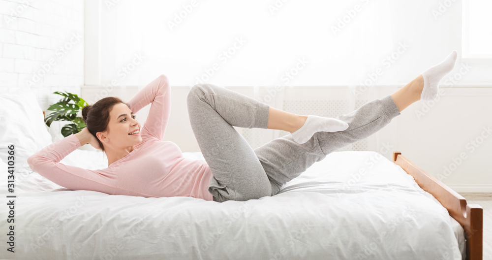 Sporty lady doing fit exercises, lying on bed at home Sporty lady doing fit exercises, lying on bed at home