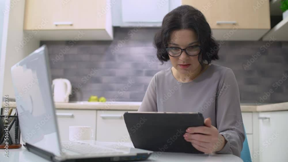 Female freelancer working on tablet, sitting in front of laptop, business career Female freelancer working on tablet, sitting in front of laptop, business career
