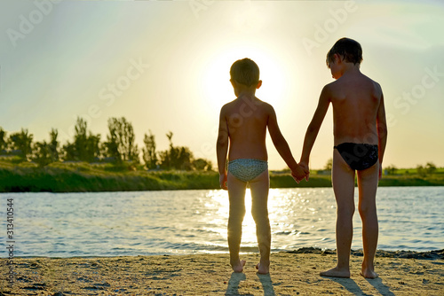 Two brothers hold hands, stand on the shore, the concept of family love. photo