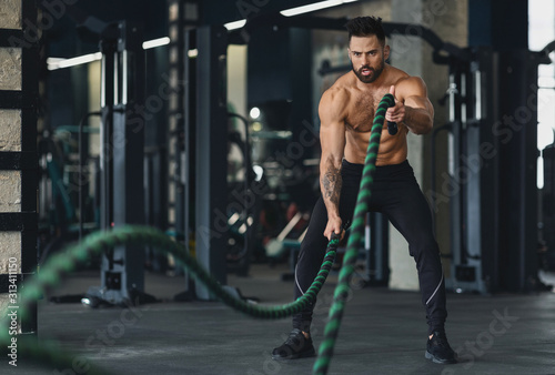 Athletic young man with battle rope doing exercise