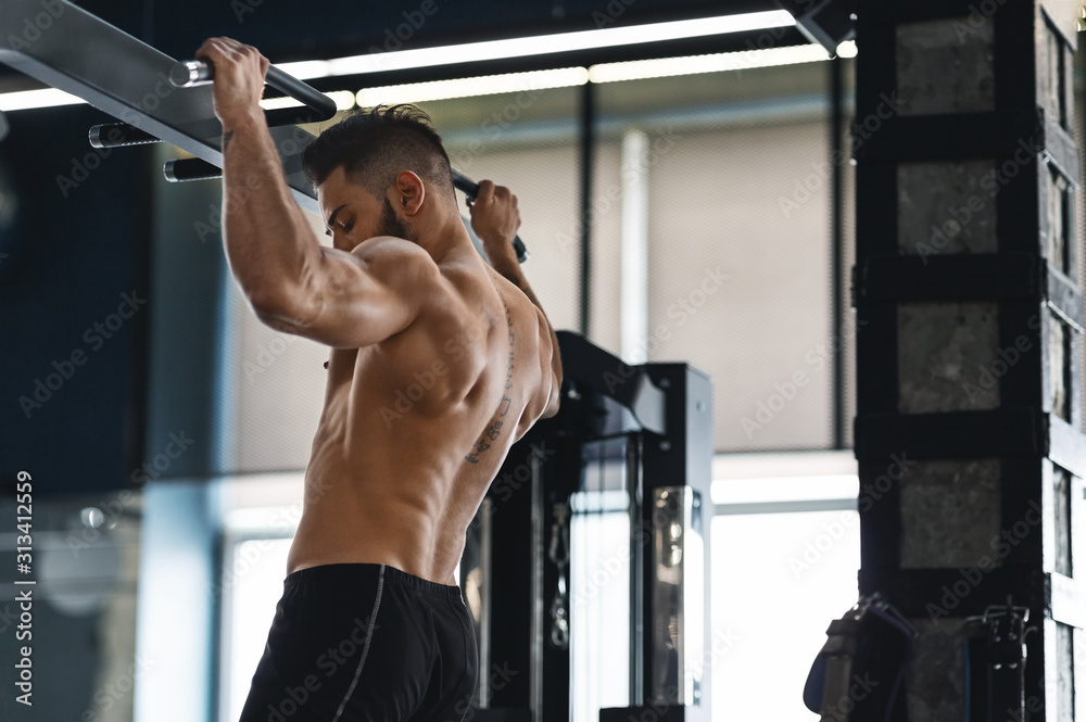 Muscular athlete pulling up on horizontal bar at gym - obrazy, fototapety, plakaty 